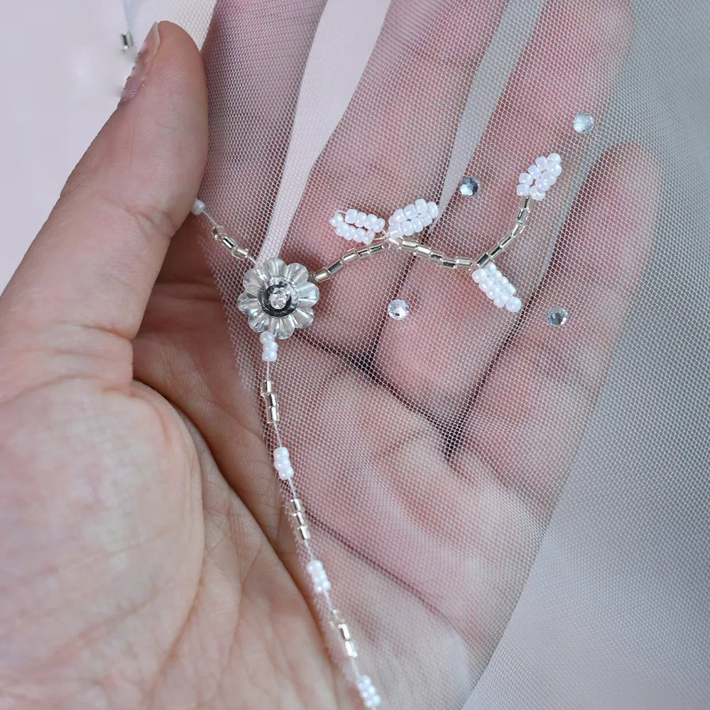 Macro close-up shot of seed beads, bugle beads, and central rhinestone forming a delicate flower spray motif on mesh