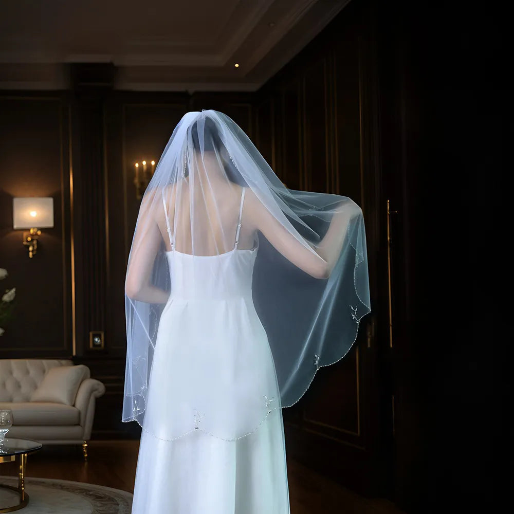 Back view of bride in white spaghetti strap gown showing 100cm veil cascading over back in moody dark room