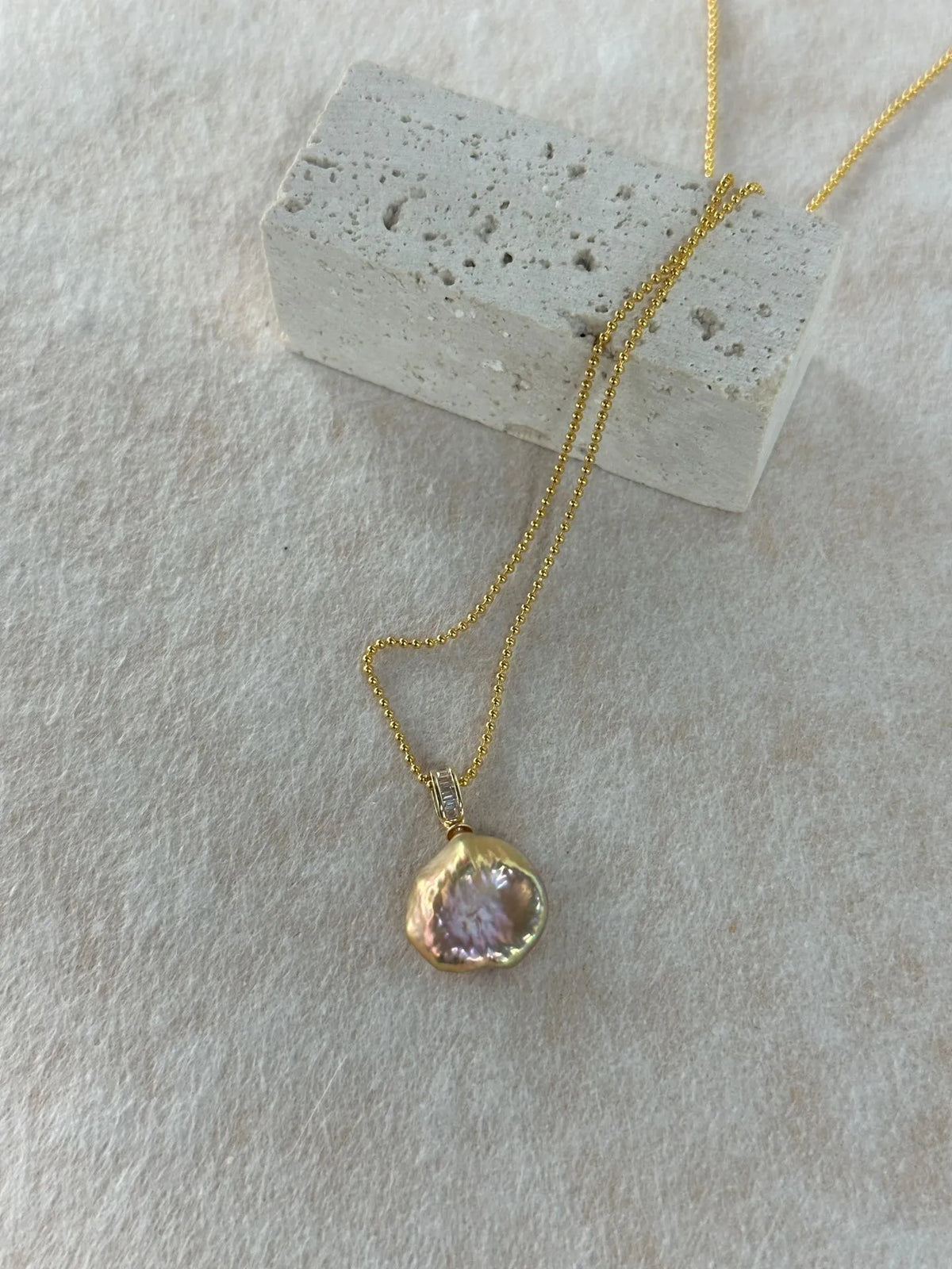18K gold plated beaded chain pearl necklace draped over a stone block prop.