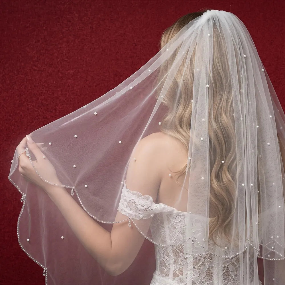 Rear view of bride in lace dress showing 2-tier scalloped beaded veil cascading over shoulders against burgundy backdrop