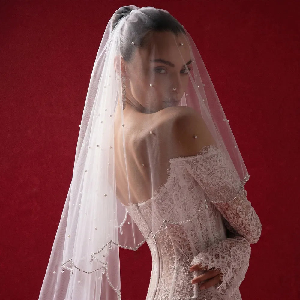 Side profile of bride with shear tulle veil draped softly over face showing scattered pearls and scalloped frame