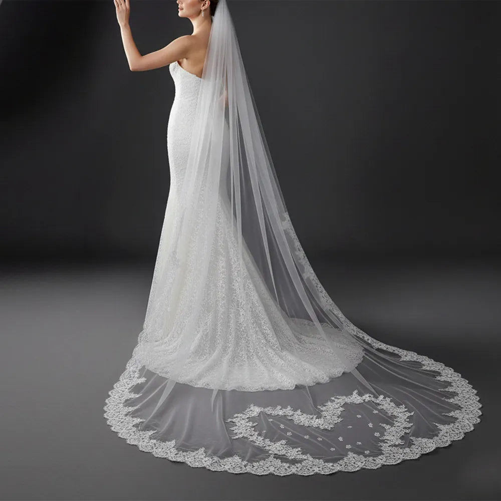 Rear silhouette of bride wearing a fitted mermaid gown as the long lace veil flows over the dress train