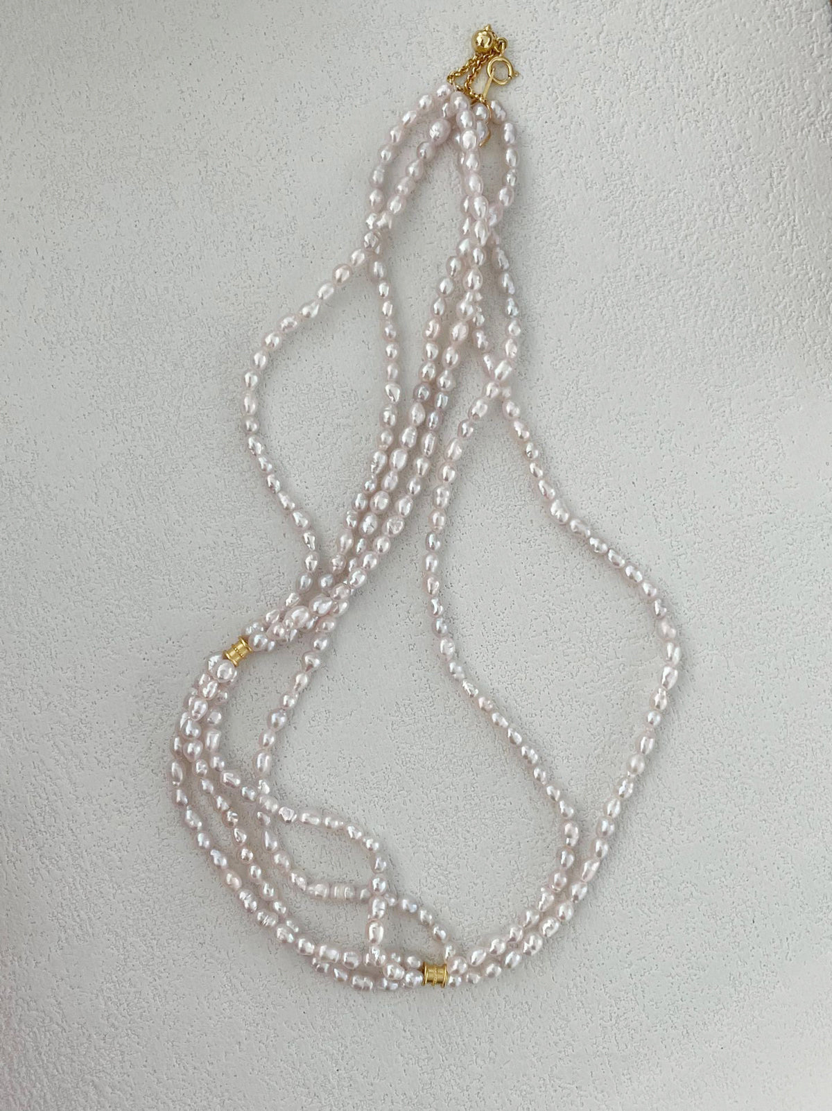 The three-strand pearl necklace styled with other delicate necklaces for a personalized layered jewelry look.