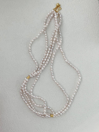 The three-strand pearl necklace styled with other delicate necklaces for a personalized layered jewelry look.