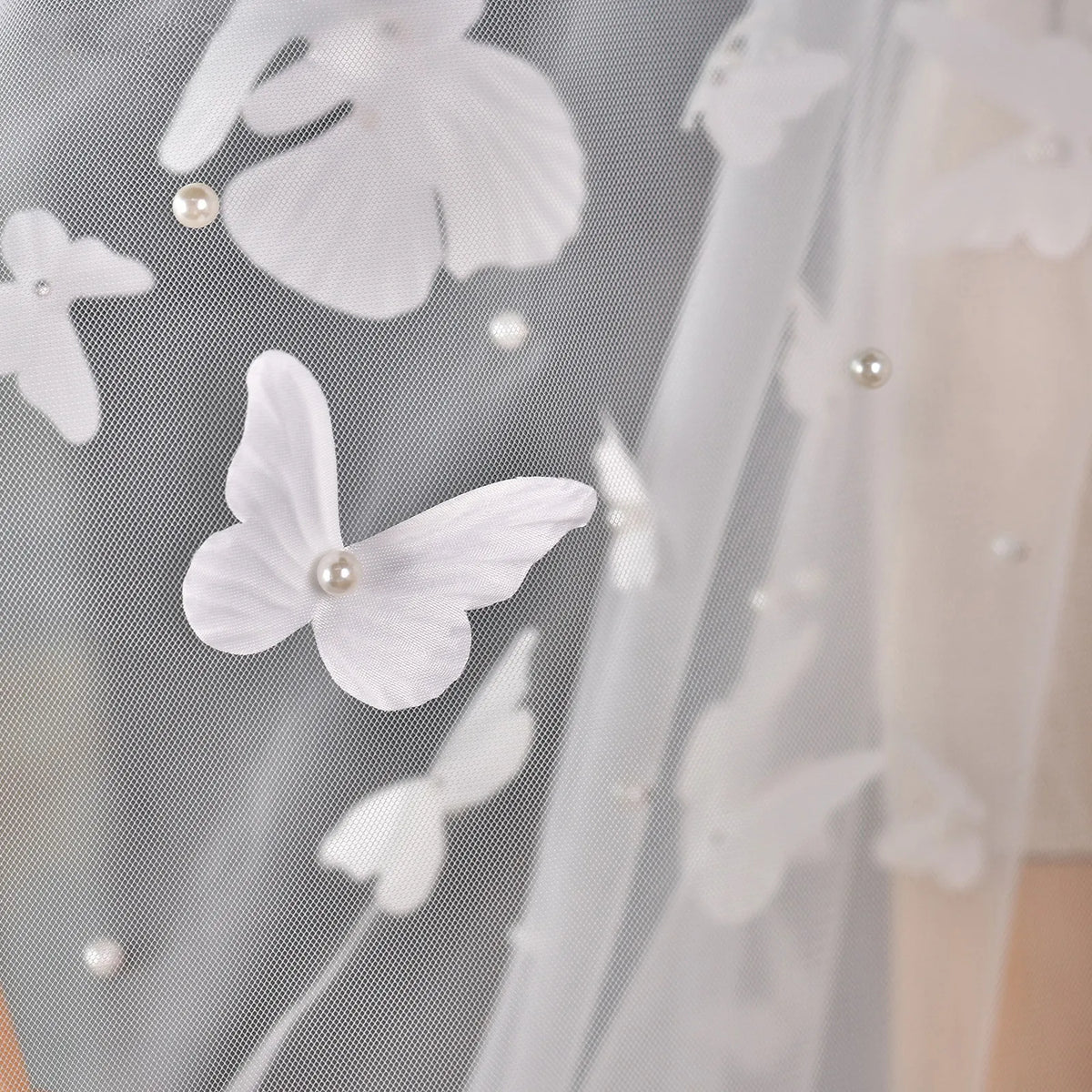Macro close-up of white 3D fabric butterfly with faux pearl center sewn onto sheer illusion bridal tulle