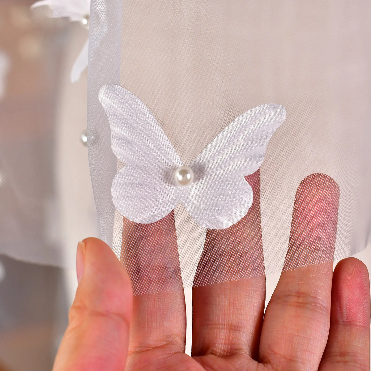 Close-up of hand holding sheer wedding veil showing 3D satin butterfly with pearl accents and delicate mesh
