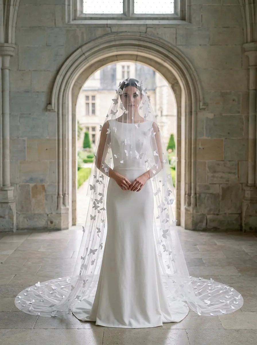 Full length front view of bride wearing 3D butterfly blusher veil draped over face in historic stone arch