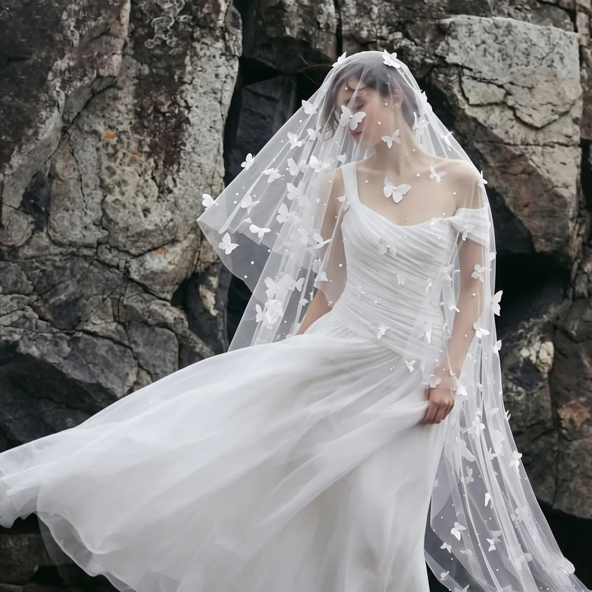Full-length windy bride portrait with flowing 3D butterfly veil and blusher against dramatic rocky coast