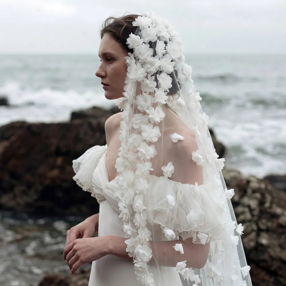 Bride in champagne satin draped dress holding out the edges of 150cm 3D flower veil against studio wall