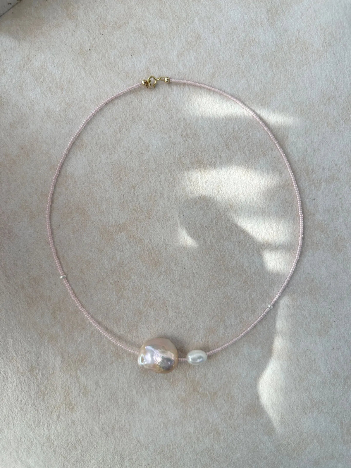 Studio shot of 40-41cm fairy pink baroque pearl necklace laid flat on soft fabric.