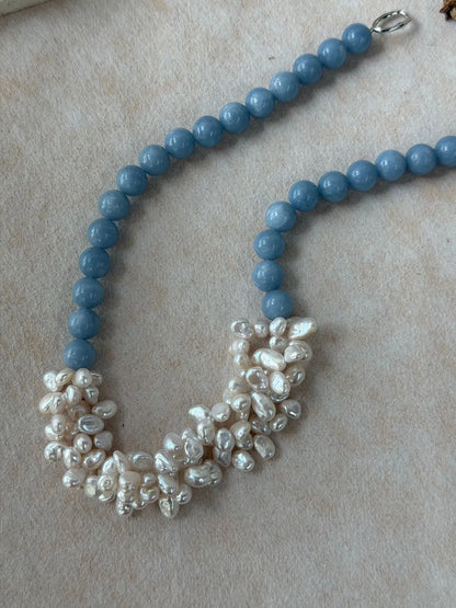 Soft blue angelite bead necklace with clustered white freshwater pearl petals displayed on beige background.
