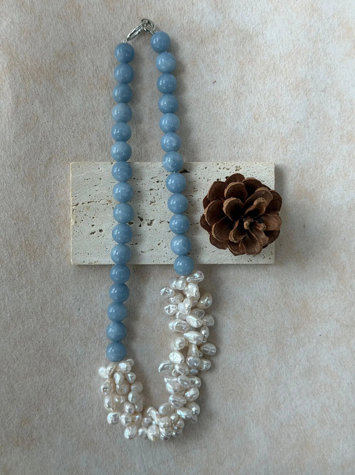 Blue angelite and baroque pearl petal necklace elegantly draped over a travertine stone block.