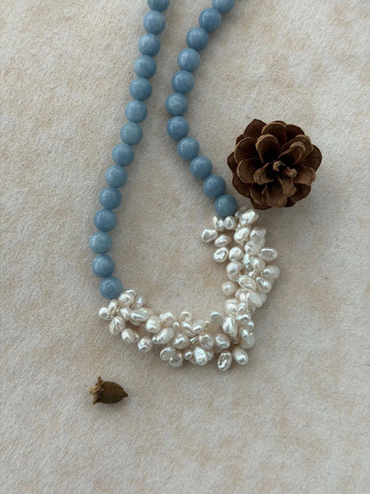 Soft blue angelite and irregular pearl cluster necklace arranged next to a natural pinecone prop.