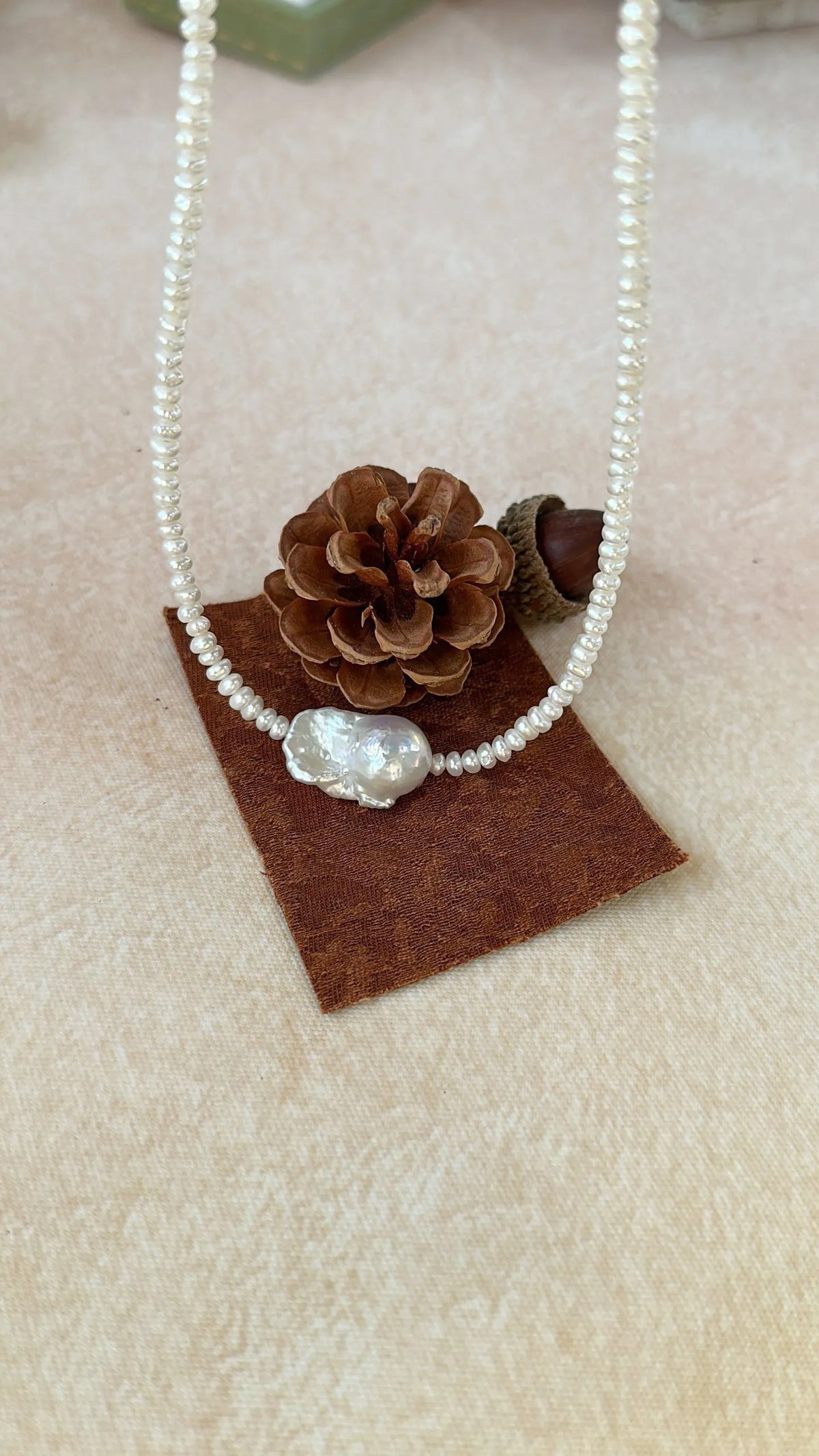 Organic baroque freshwater pearl choker necklace laid flat on a pinecone and brown pad.