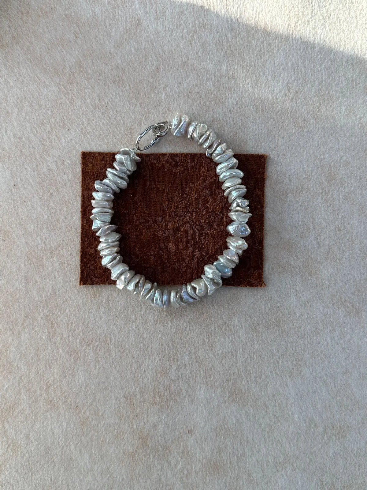 Single strand baroque freshwater pearl bracelet with S925 silver clasp on brown fabric display.