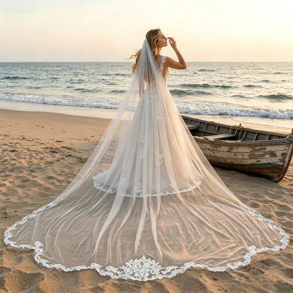 Full length back view of bride on sandy beach next to rustic boat with sweeping 350cm baroque lace veil