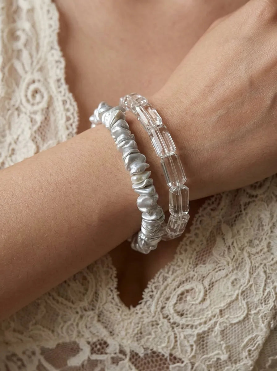 Close-up of baroque pearl and clear crystal bracelets stacked together on a wrist.