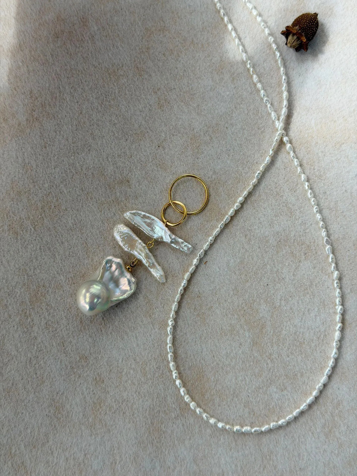Close-up view of the statement baroque pearl cluster pendant next to the fine seed pearl chain.
