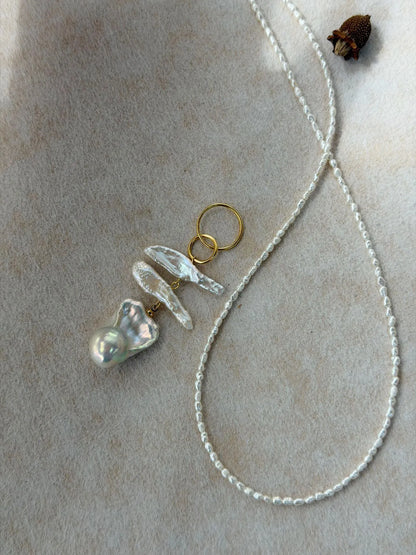 Close-up view of the statement baroque pearl cluster pendant next to the fine seed pearl chain.