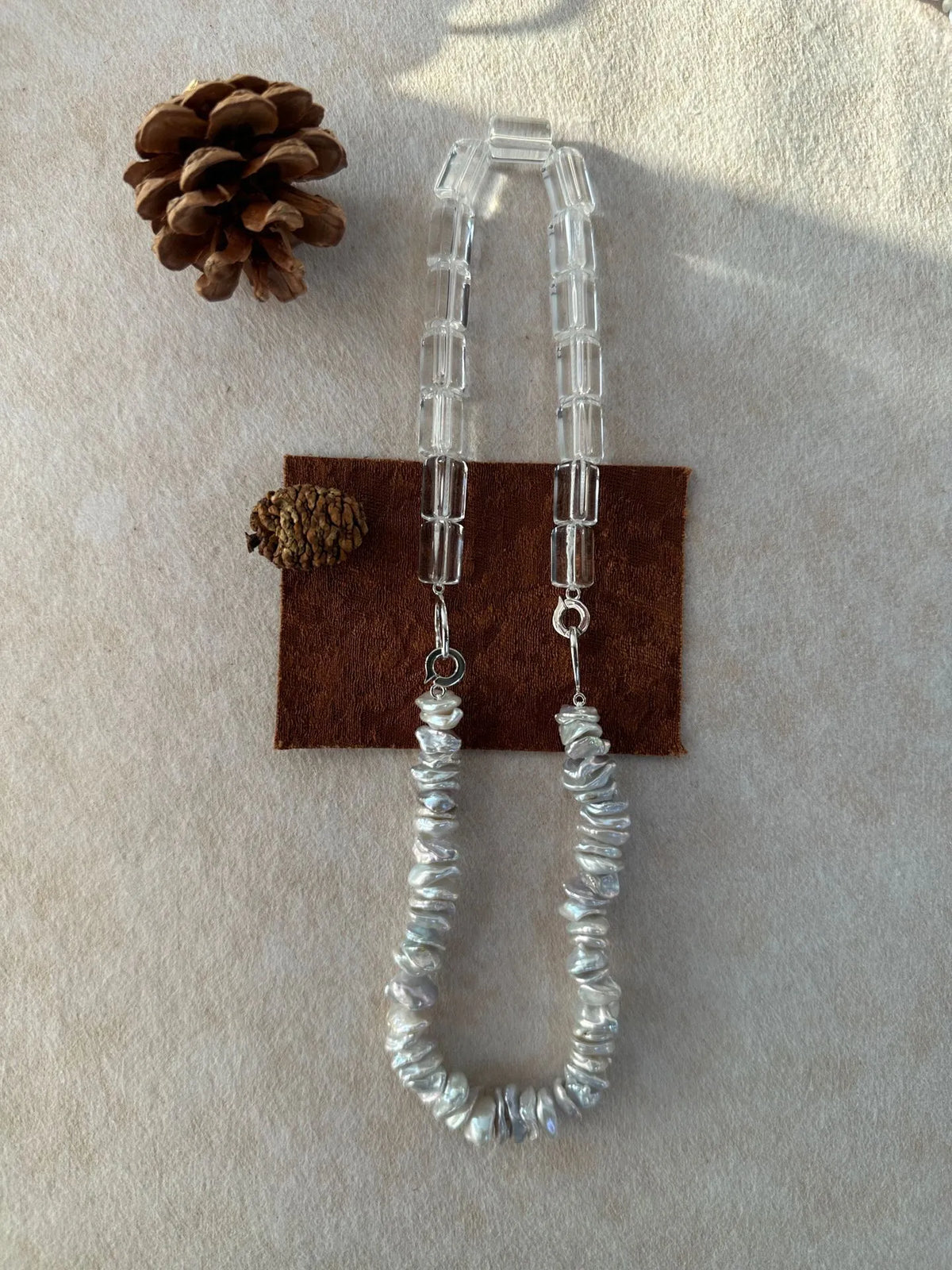 Baroque pearl and geometric crystal necklace displayed with a pinecone prop on soft cloth.