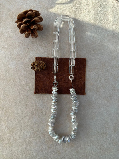 Baroque pearl and geometric crystal necklace displayed with a pinecone prop on soft cloth.