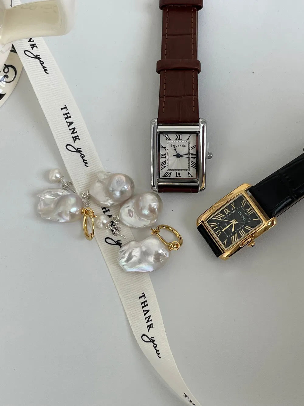 Tailed baroque pearl earrings flatlay alongside vintage leather wristwatches.