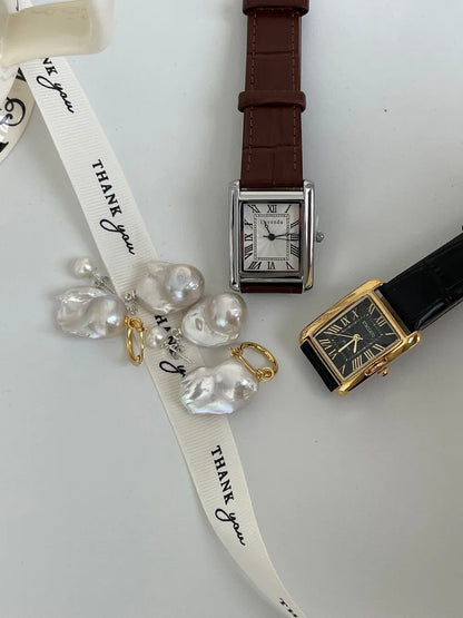 Tailed baroque pearl earrings flatlay alongside vintage leather wristwatches.