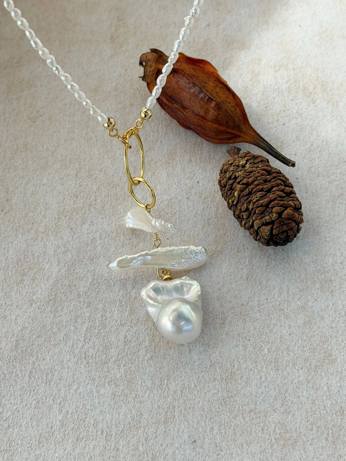 Geometric double-ring baroque pearl necklace displayed alongside rustic natural props.