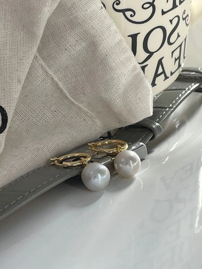 Crystal baroque pearl huggie earrings displayed alongside a gray leather watch strap and linen pouch.