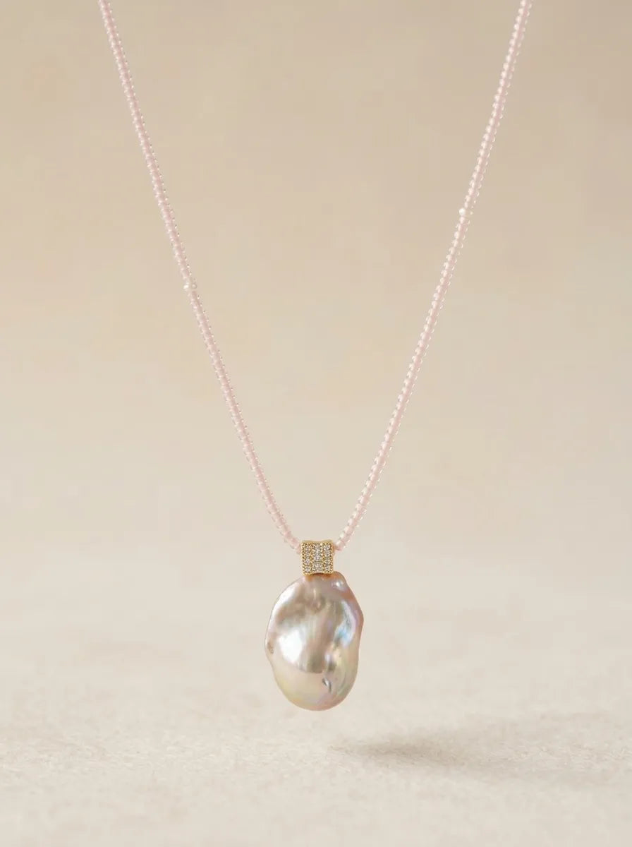 High-luster freshwater baroque pearl pendant on pink micro-bead chain against beige background.