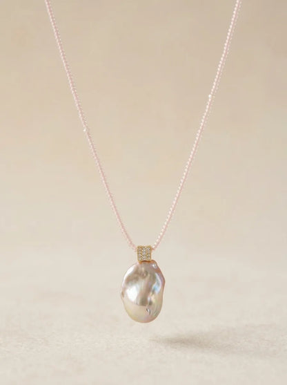 High-luster freshwater baroque pearl pendant on pink micro-bead chain against beige background.