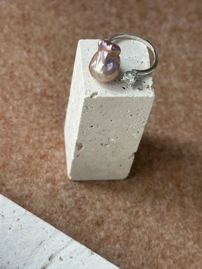 Bean baroque pearl and sparkling CZ open ring displayed on travertine stone pedestal.