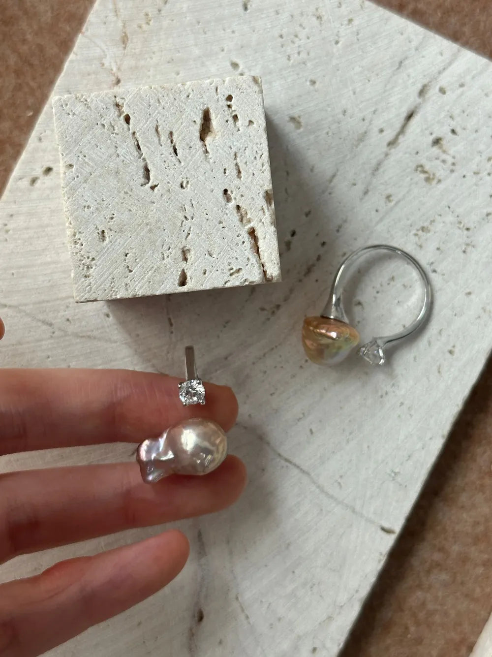 Hand holding the S925 sterling silver bean baroque pearl solitaire cz ring above travertine slab.