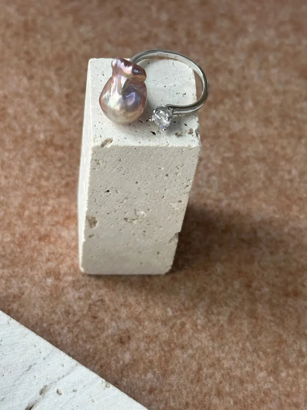Bean baroque pearl solitaire CZ ring standing on a square travertine stone display.