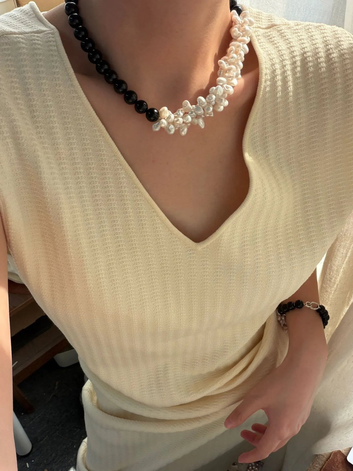 Model wearing the 43cm black onyx and clustered white pearl necklace with a V-neck knit top.