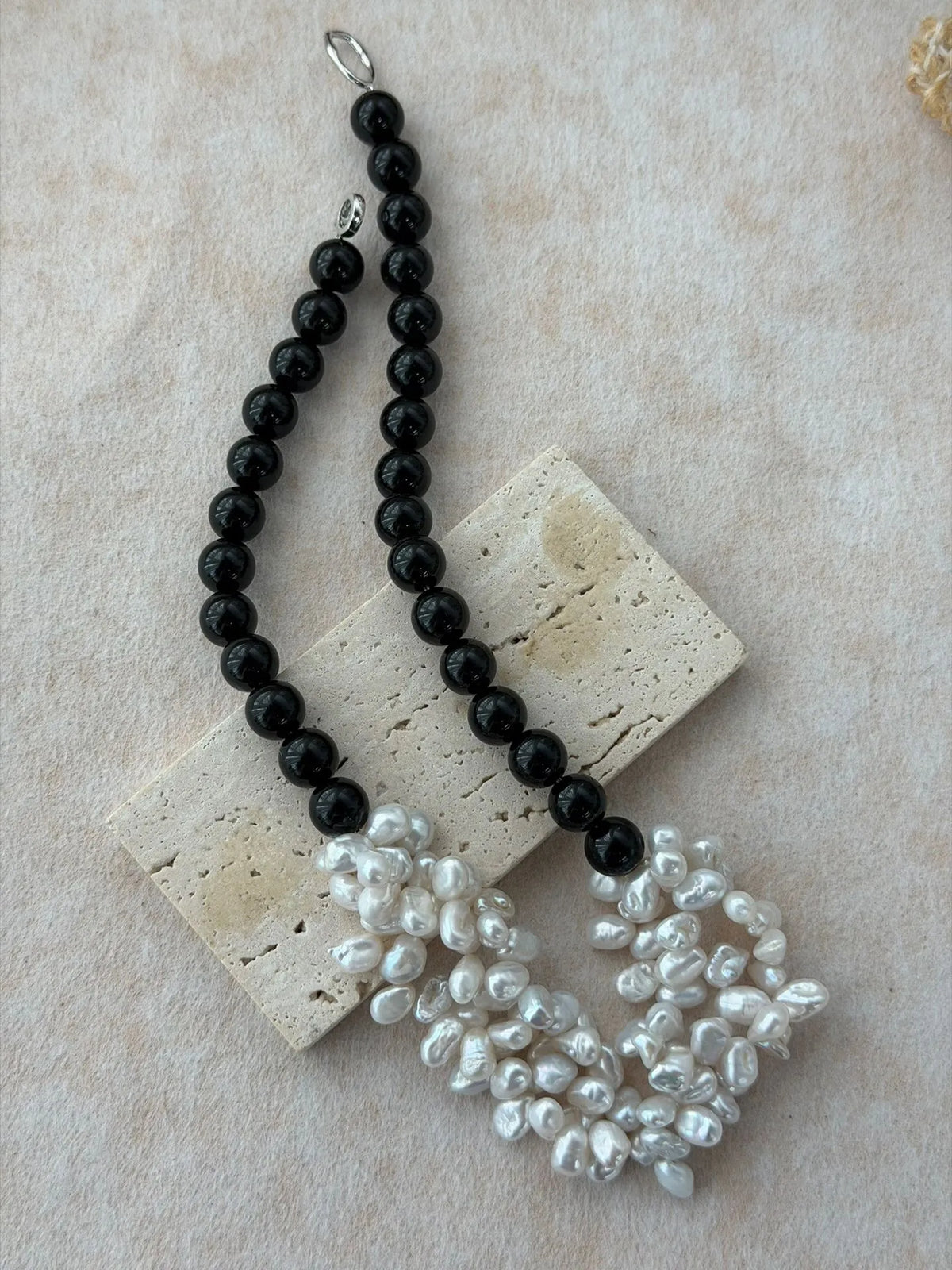 Black onyx round bead necklace with clustered white freshwater pearl petals, displayed on a sandstone stone block.