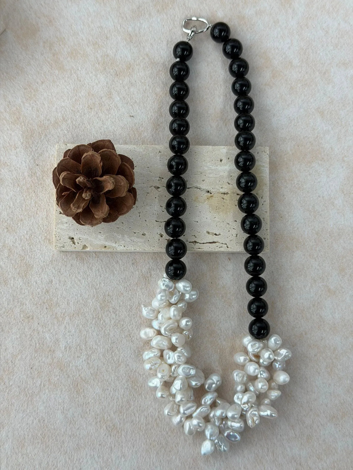 Black onyx and irregular pearl petal necklace arranged next to a natural pinecone and stone tile.