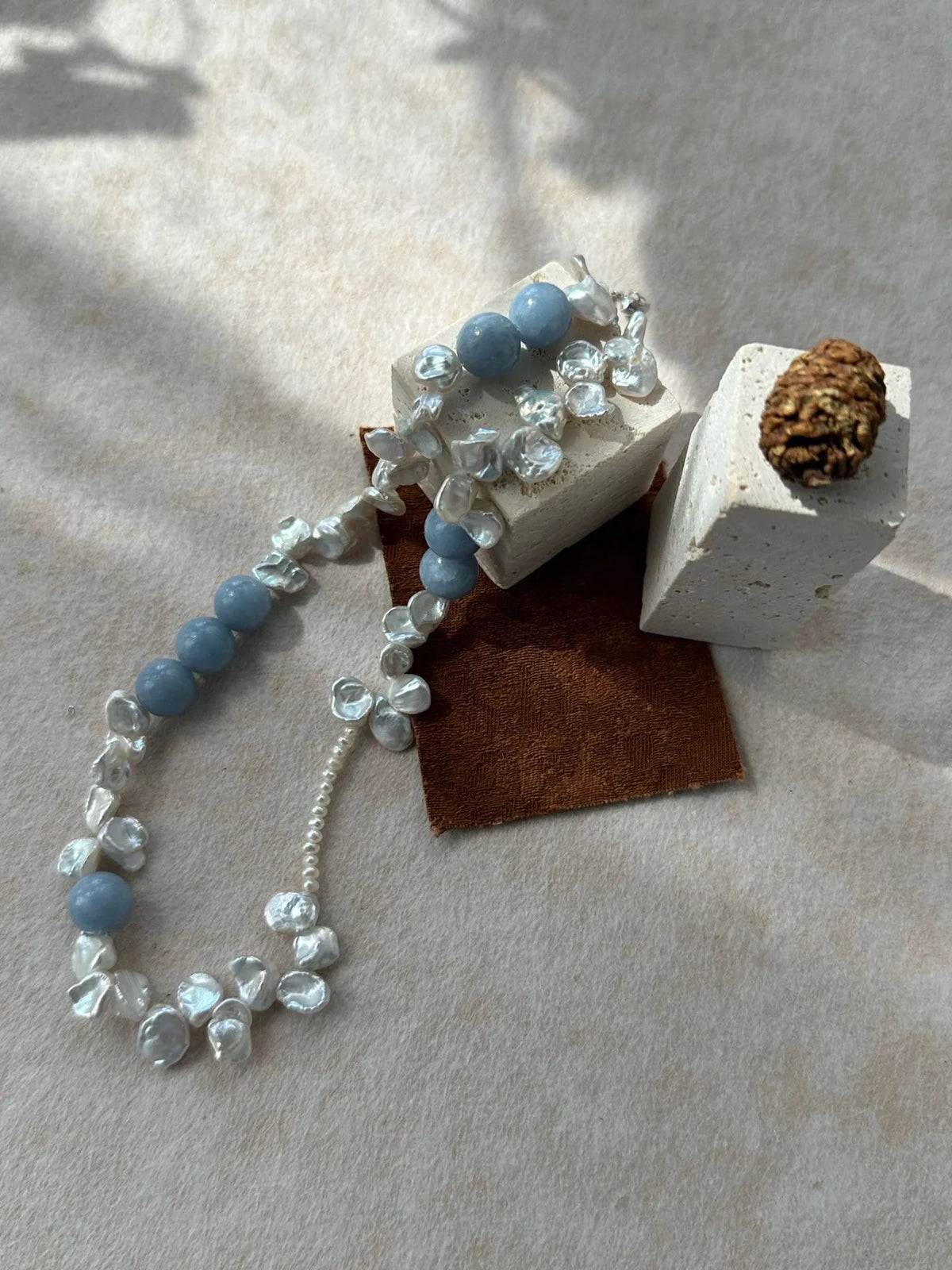 High-angle studio detail shot of blue gemstone beads and iridescent petal pearls.