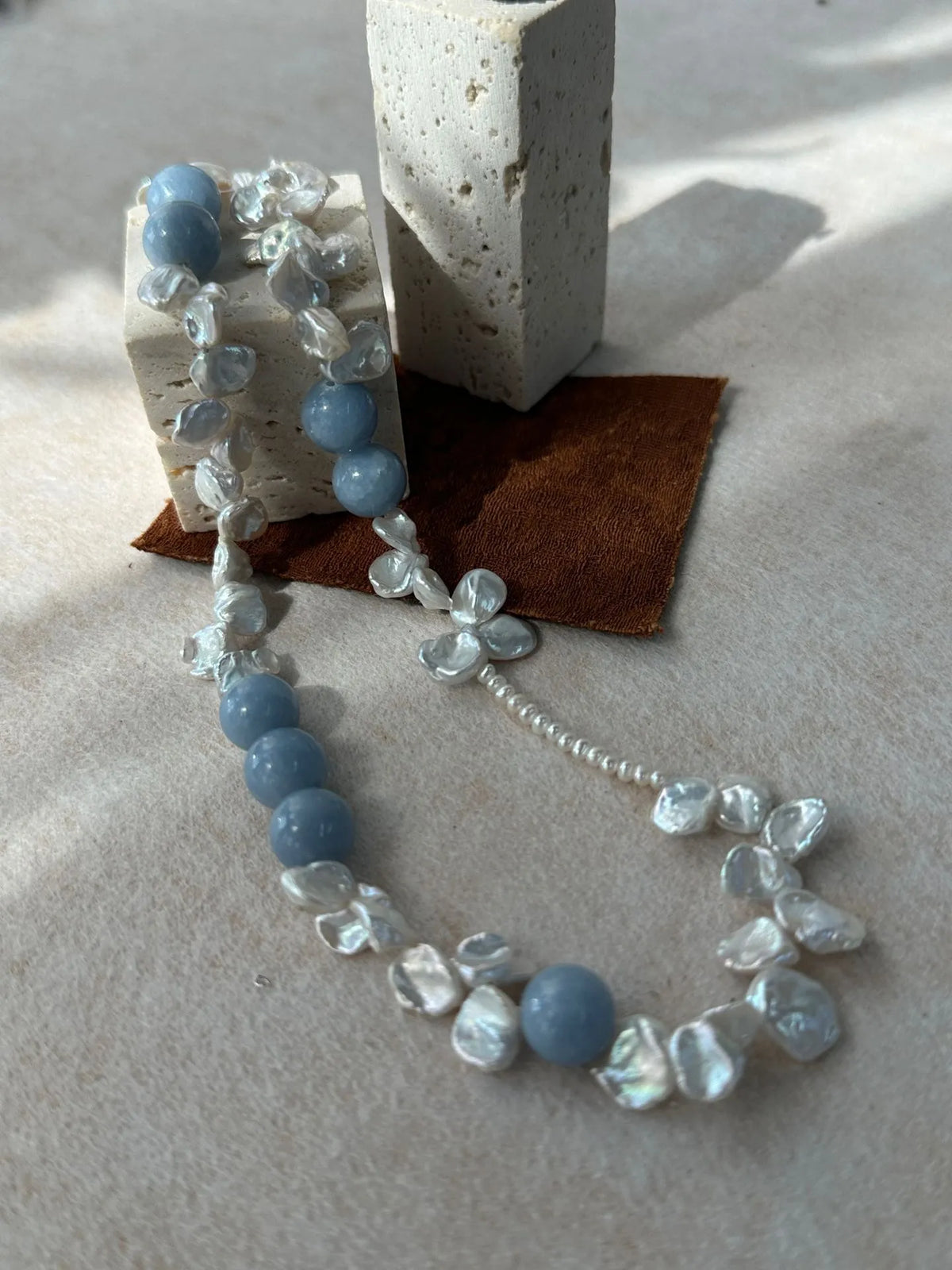 Close-up of petal baroque pearls and blue gemstone beads draped over stone display blocks.