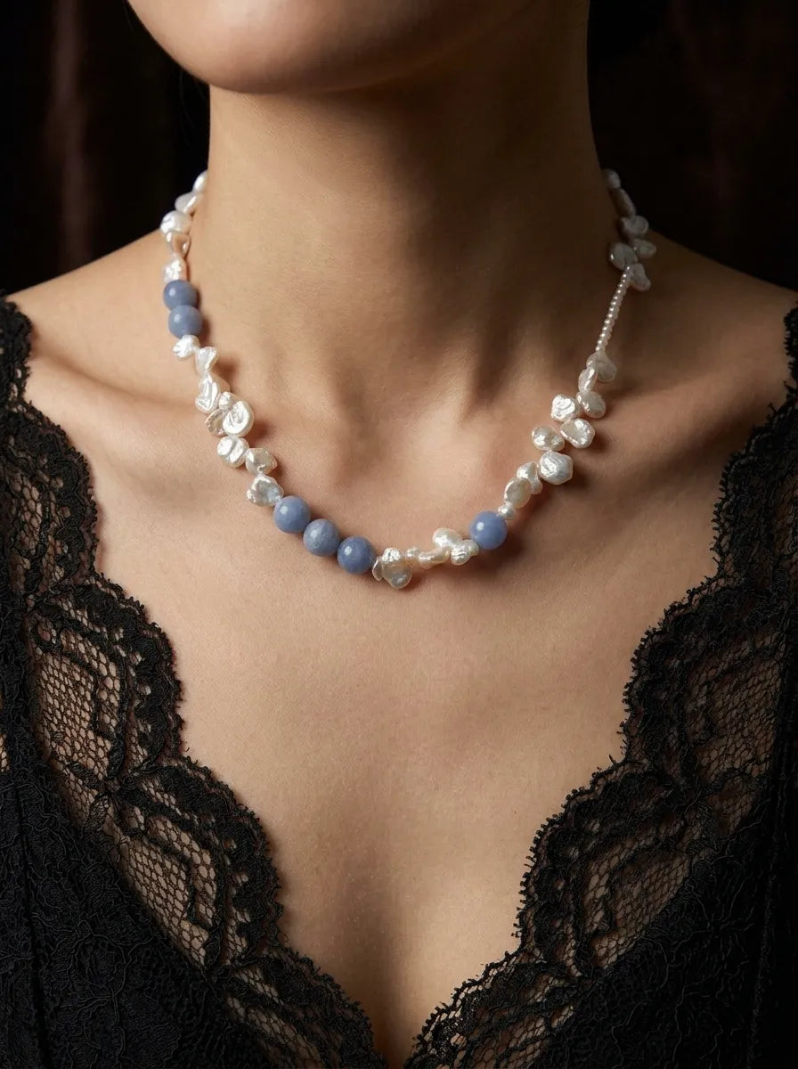Model wearing blue gemstone and freshwater petal pearl necklace with a black lace dress