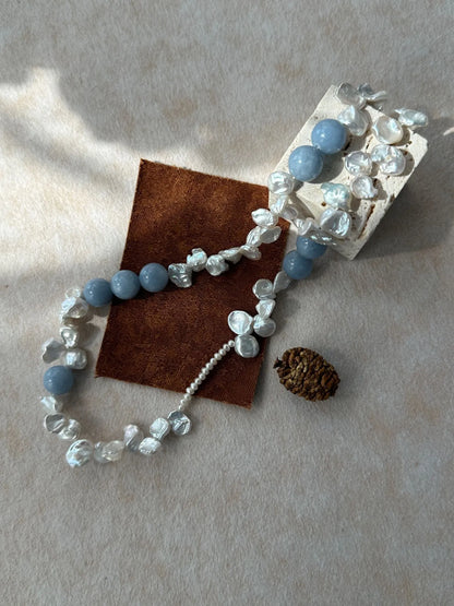 Blue gemstone and petal pearl choker displayed on stone block props with pinecone.