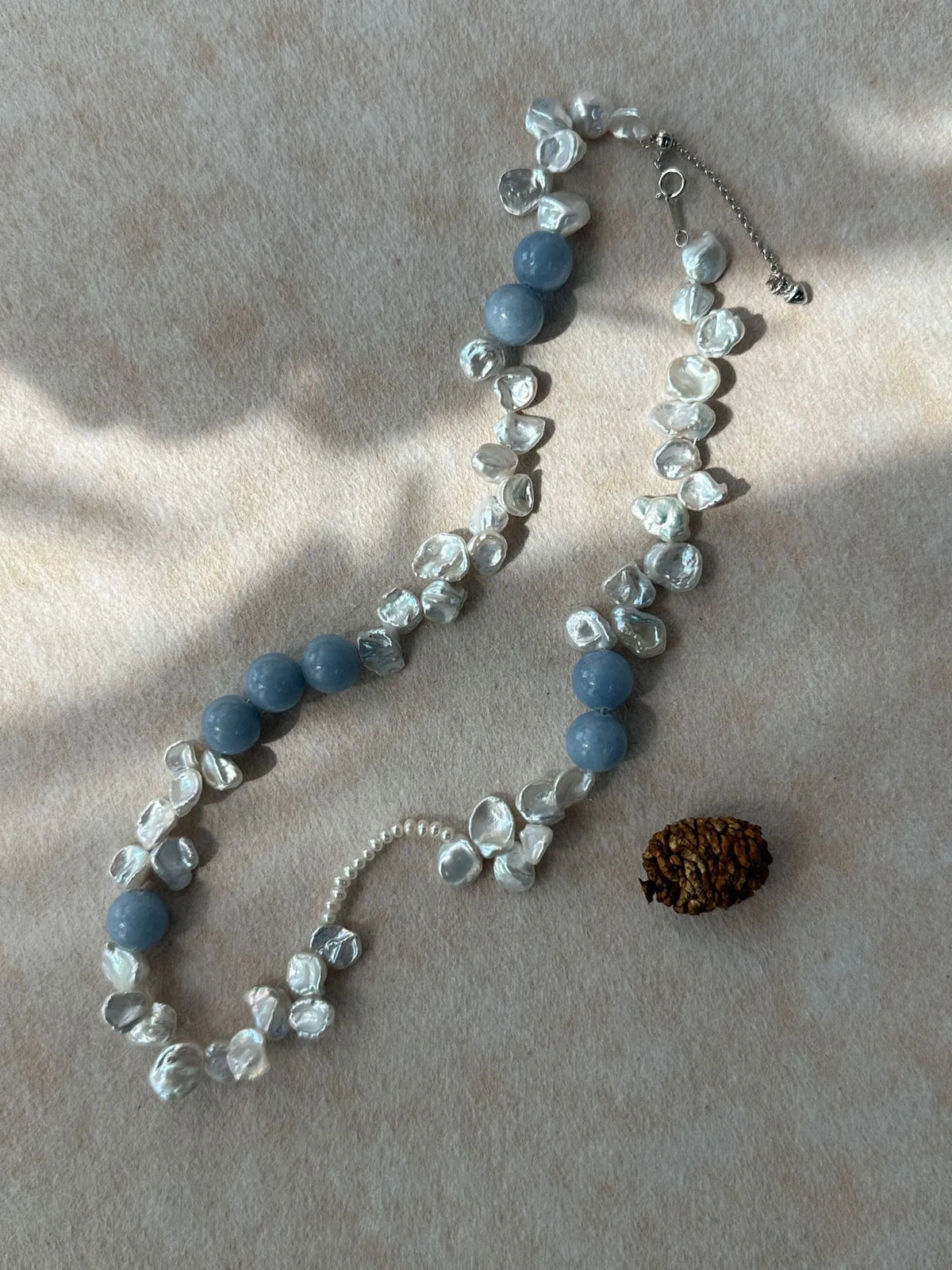 Studio flatlay of blue gemstone and petal pearl choker under soft natural sunlight