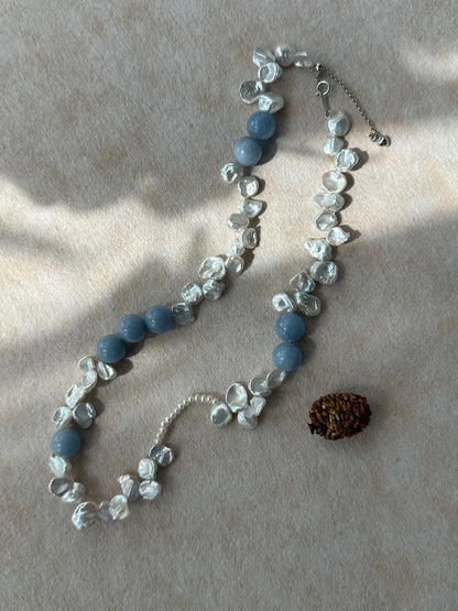 Studio flatlay of blue gemstone and petal pearl choker under soft natural sunlight