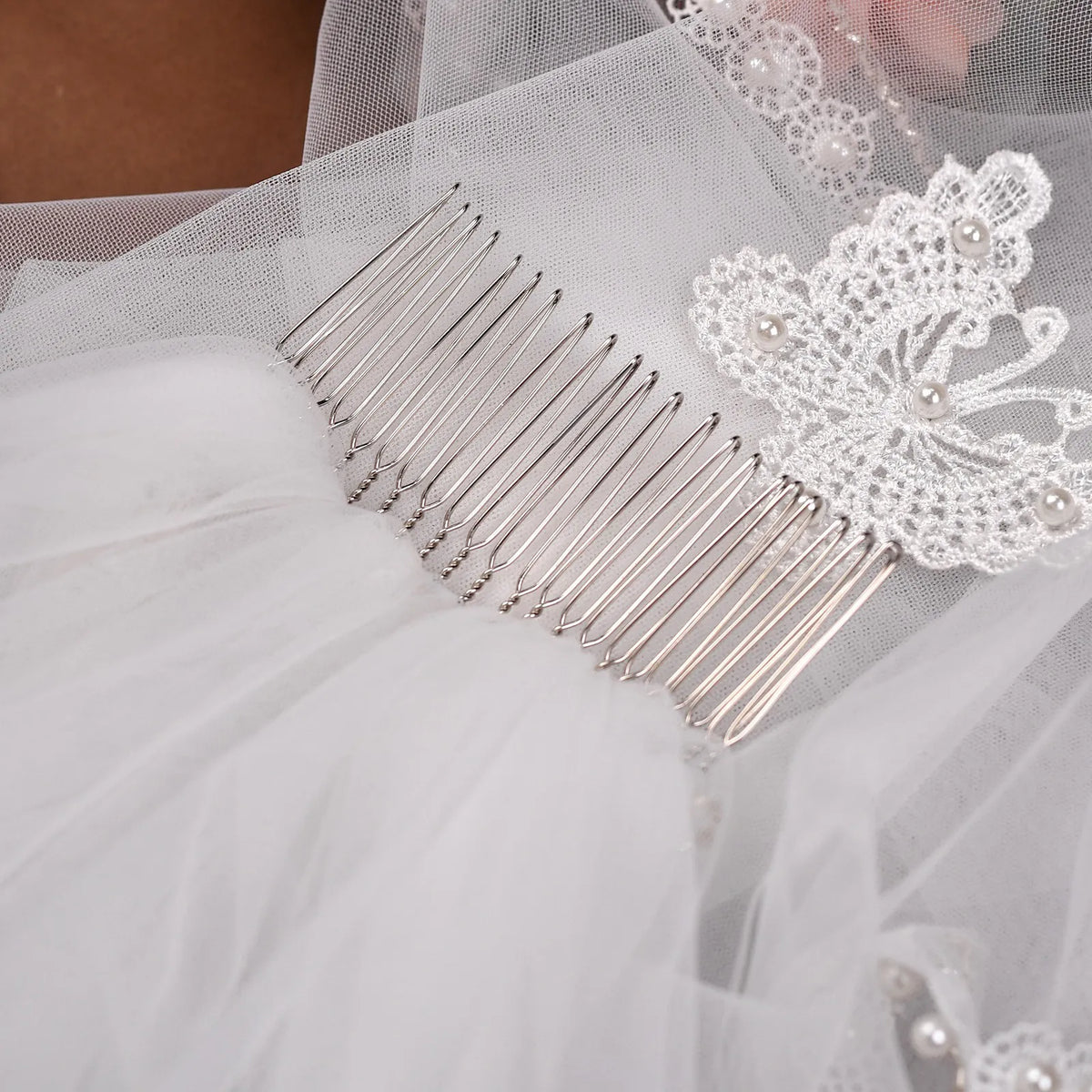 Extreme close-up photo of sturdy silver metal hair comb stitched under soft white tulle and pearl butterfly lace accent
