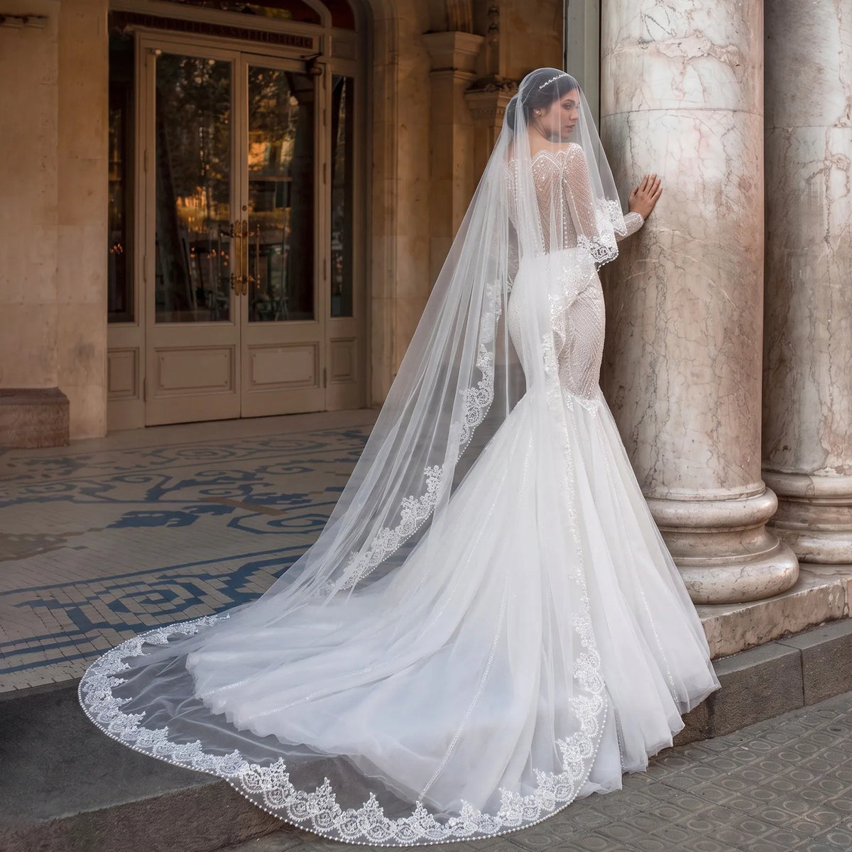 Side view of bride in mermaid lace wedding dress wearing a 300cm cathedral veil with ornate lace and pearl edge sweeping across stone floor