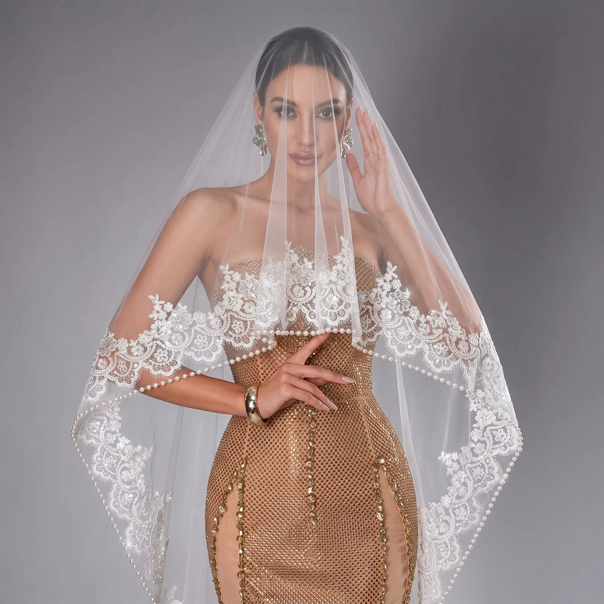 Front close-up view of bride with sheer veil over face, showcasing intricate floral lace appliques and dangling pearl beaded border