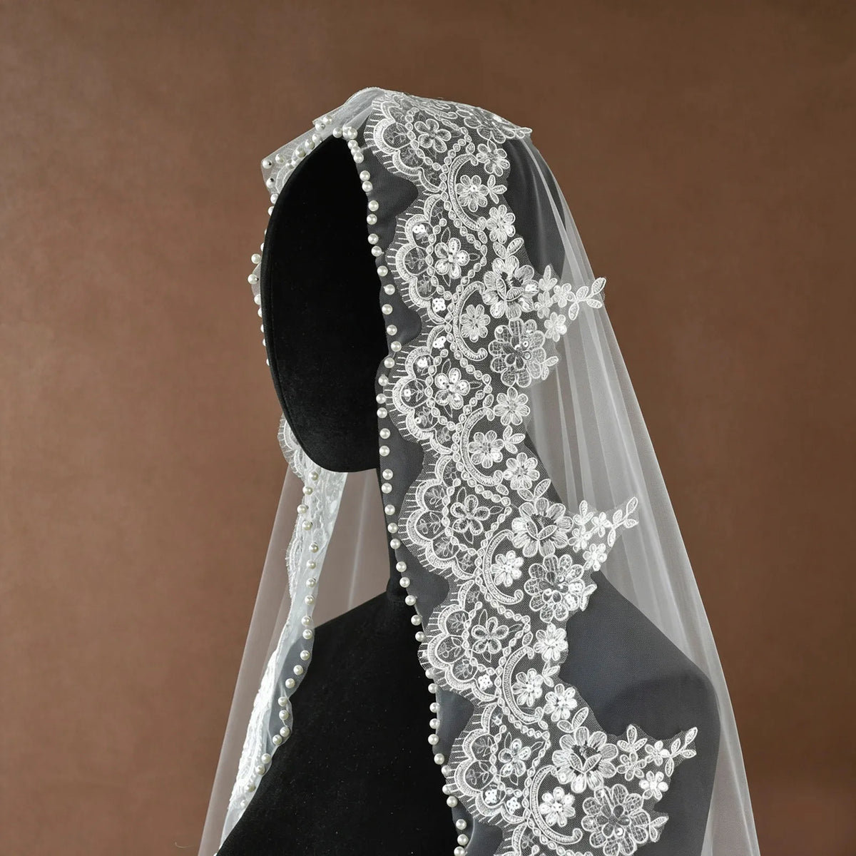 Three-quarter angle view of veil on mannequin showing rich lace border and fluid cascading tulle falling to the wooden floor