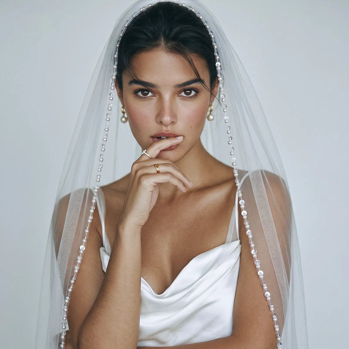 Half-length front view of bride in satin corset wedding dress with transparent veil draped over head and subtle shimmering sequin border down both sides
