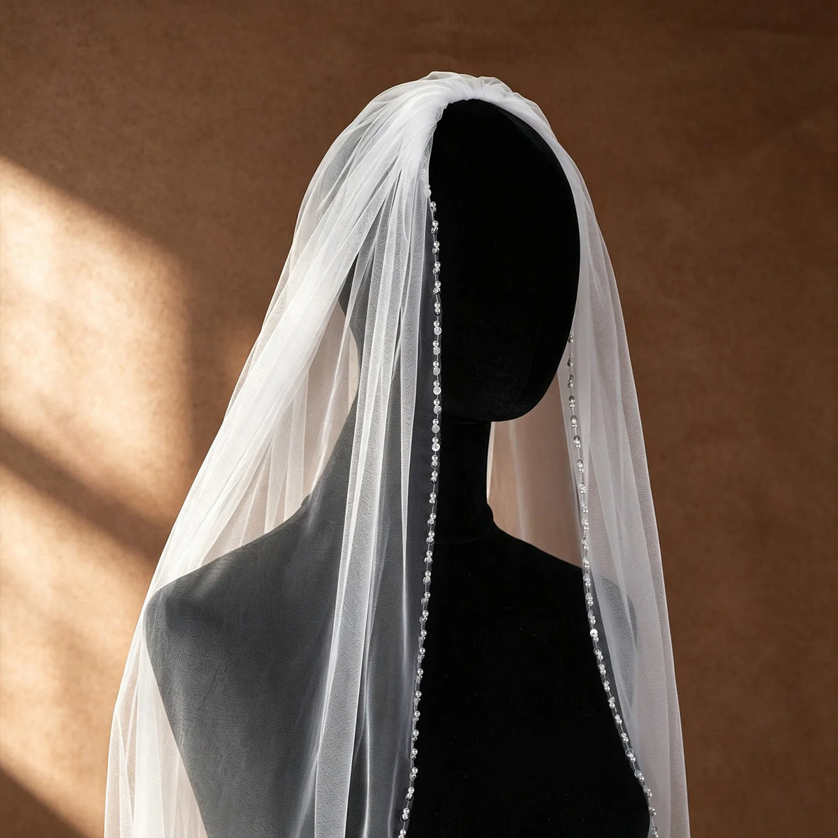 Close-up side profile of veil mounted on a black mannequin, displaying delicate gathered tulle and precise sequin pearl border details
