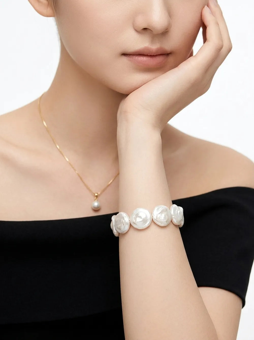 Model holding hand to chin displaying the coin baroque pearl bracelet on wrist.